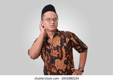 Portrait of attractive Asian man wearing batik shirt and songkok scratching neck. Allergies symptoms. Isolated image on gray background