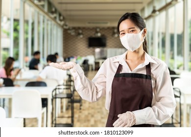 Portrait Attractive Asian Waitress Wear Face With Background Of Customers Sit In Social Distance Table In Restaurant Indoor. New Normal Restaurant Lifestyle Concept.