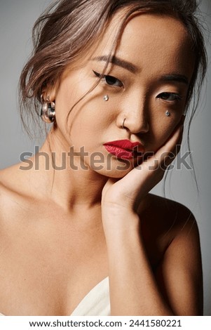 portrait of attractive asian young woman covering cheek with hand against grey background