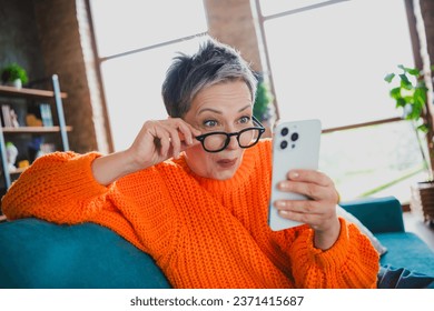 Portrait of attractive astonished lady sit sofa arm touch eyewear use smart phone read news apartment indoors - Powered by Shutterstock