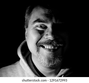 Portrait of attractive bearded adult caucasian man. He smiles like maniac and seems like madness. Black and white shot, low-key lighting. Isolated on black.
