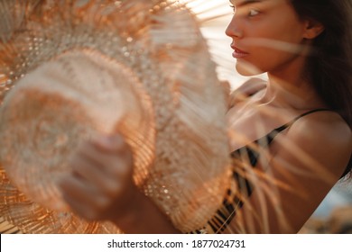 Portrait of attractive blonde girl woman with long hair posing on rocky beach on sunset background,  hold straw hat in her hands and look at the sea - Powered by Shutterstock