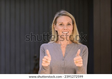 Portrait of an attractive blonde woman giving a double thumbs up gesture, in front of wooden wall