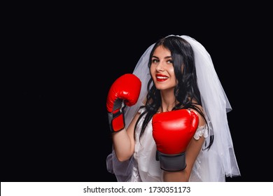 Portrait Of An Attractive Brunette With Red Lipstick, In Wedding Dress, Veil And Boxing Gloves. Young Girl In Role Of A Bride On A Black Background, Standing In A Boxing Stand, Smiling At Camera