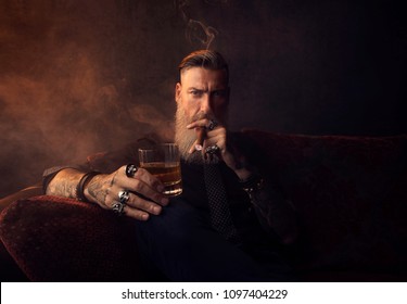 Portrait Of An Attractive Business Man With A Cigar And A Glass Of Whiskey In A Dark Room