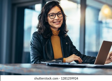 Portrait of attractive business woman sitting at her desk with laptop computer in office. Smiling business woman in casuals at office.
