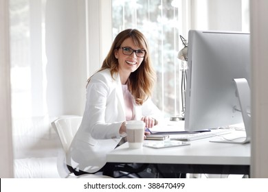 Portrait Of Attractive Businesswoman Sitting At Her Desk Looking Happy While Working At Office In Front Of Computer.