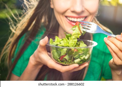 Portrait of attractive caucasian smiling woman eating salad, focus on hand and fork. soft, backlight - Shutterstock ID 288126602