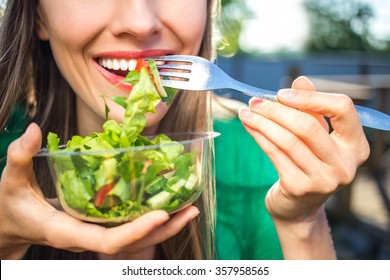 Portrait of attractive caucasian smiling woman eating salad, focus on hand and fork. soft, backlight - Shutterstock ID 357958565