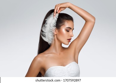 Portrait of attractive Caucasian woman with raised hand. beautiful young girl holds feather in hands and looks at armpit. Smooth clean skin of the face and body. concept care, epilation armpit