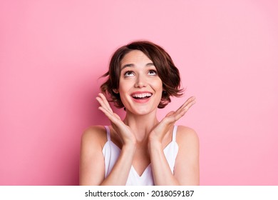 Portrait of attractive cheerful amazed brown-haired girl looking up copy space isolated over pastel pink color background