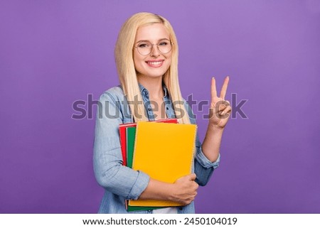 Portrait of attractive cheerful brainy girl holding book showing v-sign isolated over shine violet purple color background