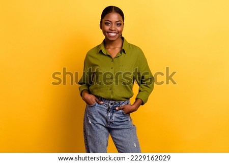 Portrait of attractive cheerful content brunette girl posing holding hands in pockets isolated over bright yellow color background