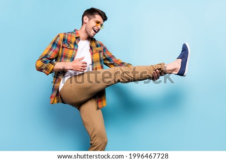 Portrait of attractive cheerful funky guy dancing having fun holding leg fooling isolated over bright blue color background