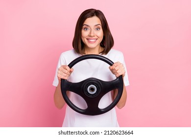 Portrait of attractive cheerful girl holding steering wheel pretending riding car isolated over pink pastel color background