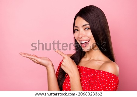 Portrait of attractive cheerful girl holding on palm demonstrating copy space ad isolated over pink pastel color background