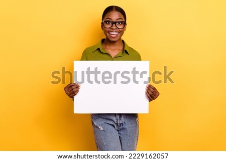 Portrait of attractive cheerful girl holding in hands copy space banner isolated over bright yellow color background