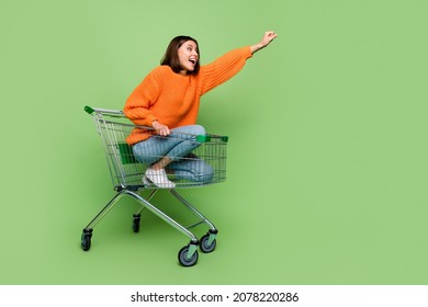 Portrait of attractive cheerful girl riding cart basket striving travel super hero isolated over bright green color background