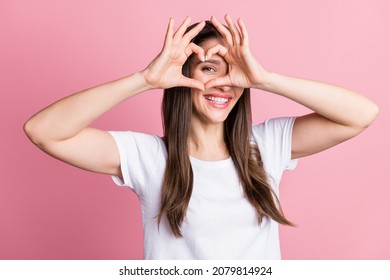 Portrait of attractive cheerful girl showing heart shape looking eye sindow spy isolated over pink pastel color background