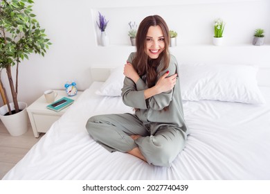 Portrait of attractive cheerful girl sitting on bed hugging herself sweet day at home house light white interior