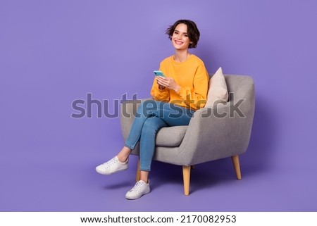 Portrait of attractive cheerful girl sitting in chair using device gadget app 5g isolated over violet lilac color background