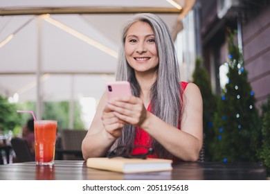 Portrait of attractive cheerful grey-haired woman using device gadget smm app 5g free time roaming sitting at cafe outdoors
