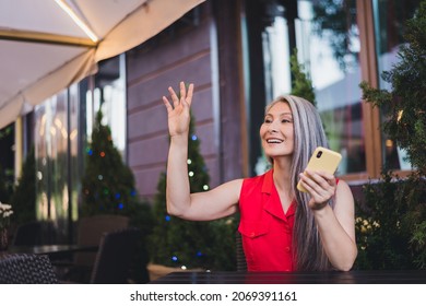 Portrait of attractive cheerful grey-haired woman sitting at cafe using device waving hi meeting boyfriend outdoors