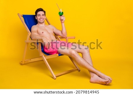 Portrait of attractive cheerful guy drinking mojito in plage isolated over bright yellow color background
