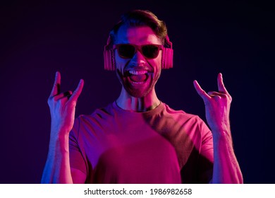 Portrait of attractive cheerful guy listening bass sound showing horn sing having fun isolated over dark neon light violet color background - Powered by Shutterstock