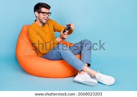 Portrait of attractive cheerful guy sitting in chair playing video game having fun free time isolated over bright blue color background