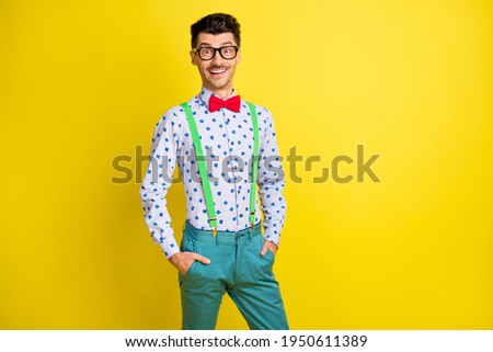 Portrait of attractive cheerful guy wearing print shirt holding hands in pockets isolated over bright yellow color background