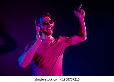 Portrait of attractive cheerful hipster guy listening bass sound single dancing isolated over dark neon light violet color background - Powered by Shutterstock