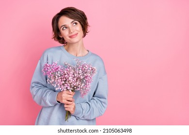 Portrait of attractive cheerful minded dreamy girl holding flowers copy space deciding isolated over pink pastel color background