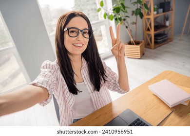 Portrait of attractive cheerful person sit chair take selfie demonstrate v-sign laptop desktop office indoors