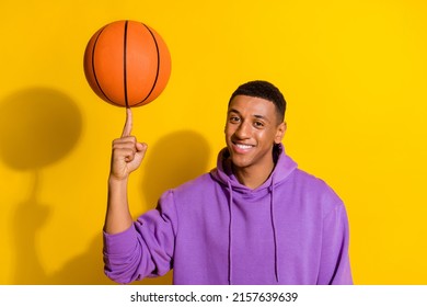 Portrait of attractive cheerful sportive guy spinning on forefinger orange ball isolated over bright yellow color background
