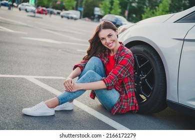 Portrait Of Attractive Cheerful Wavy-haired Girl Driver New Car Owner Sitting On Floor Resting Weekend Good Mood On Parking Outdoors