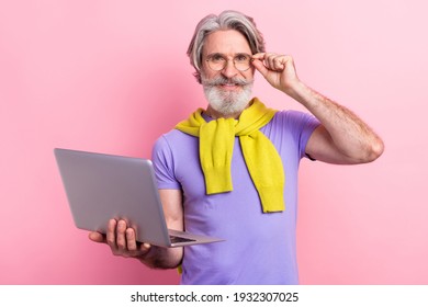 Portrait of attractive cheery skilled gray-haired man holding on palm using laptop touching specs isolated on pink pastel color background - Shutterstock ID 1932307025