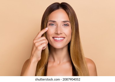 Portrait of attractive cheery woman touching under eye lifting uplift laser peeling effect isolated over beige pastel color background