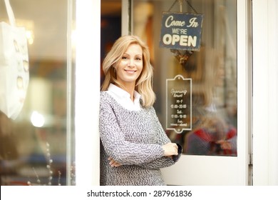 Portrait of attractive clothing store owner standing in her shop entrance. Small shop owner looking at camera and smiling. 