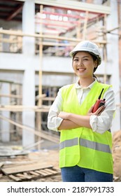 Portrait Of An Attractive And Confident Young Asian Female Engineer In Uniform And White Hardhat Standing In The Construction Site.