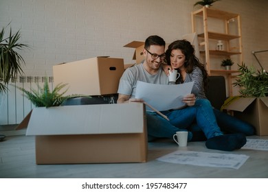 Portrait of attractive couple analyzing plans for a new home while having coffee on the floor. Cardboard boxes all around them. - Powered by Shutterstock