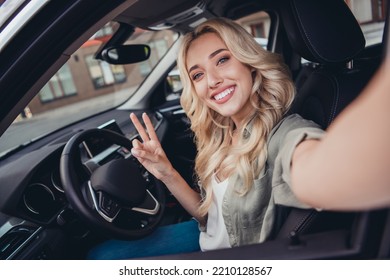 Portrait of attractive curly person sitting car driver seat make selfie hand fingers demonstrate v-sign