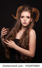 Portrait of an attractive demon woman with horns and curly hair, wooden cup, studio shot for Halloween