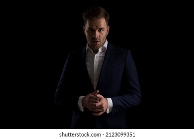 Portrait Of Attractive Fashion Man In Navy Blue Suit Rubbing Palms And Posing On Black Background In Studio