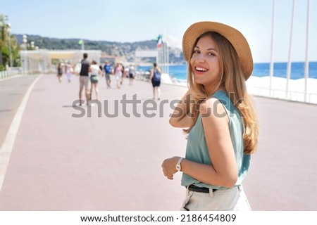 Portrait of attractive fashion woman turns around and smiling at camera walking along Promenade des Anglais, Nice, France