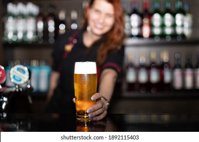 Portrait of attractive female bartender tapping beer in pub, focus on hands holding beer - Powered by Shutterstock