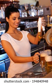 Portrait Of Attractive Female Bartender Tapping Beer In Bar, Smiling.
