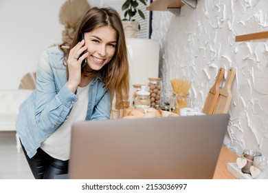 Portrait of attractive female freelancer or student sitting at the chair, looking at camera and using laptop. Beautiful business woman talking with coworker by the phone, smiling, discussing project. - Powered by Shutterstock