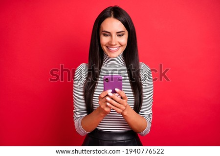 Portrait of attractive focused cheerful long-haired girl browsing media isolated over bright red color background