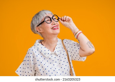 Portrait of attractive funky asian tattoo cheerful grey-haired elder old senior woman touching spectacles isolated over yellow pastel background color,surprise and over exited feeling expression
